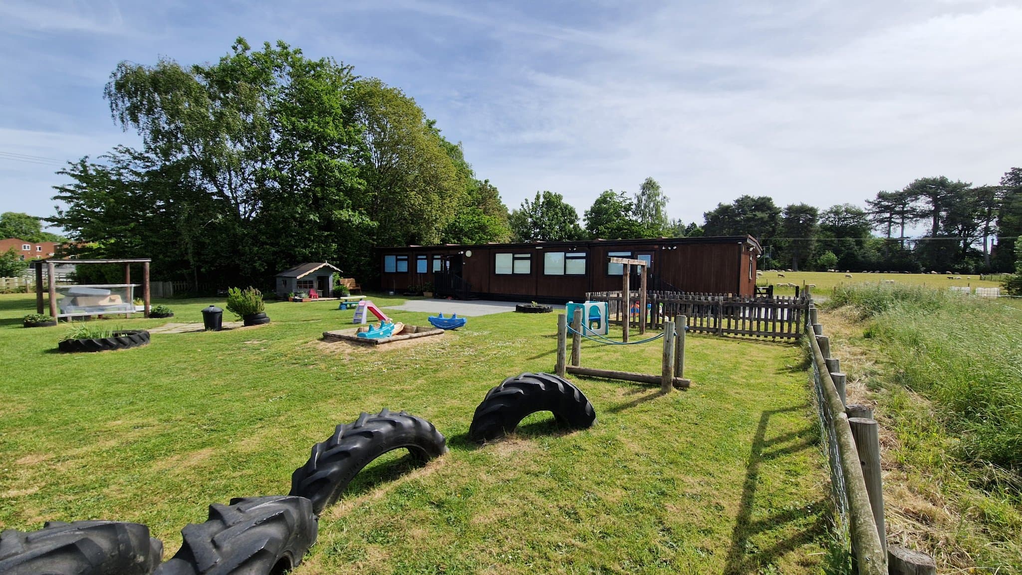 Exterior of the purpose-built Bojangles Day Nursery in Baschurch — single-storey timber building set in its garden grounds with play equipment and open Shropshire countryside beyond