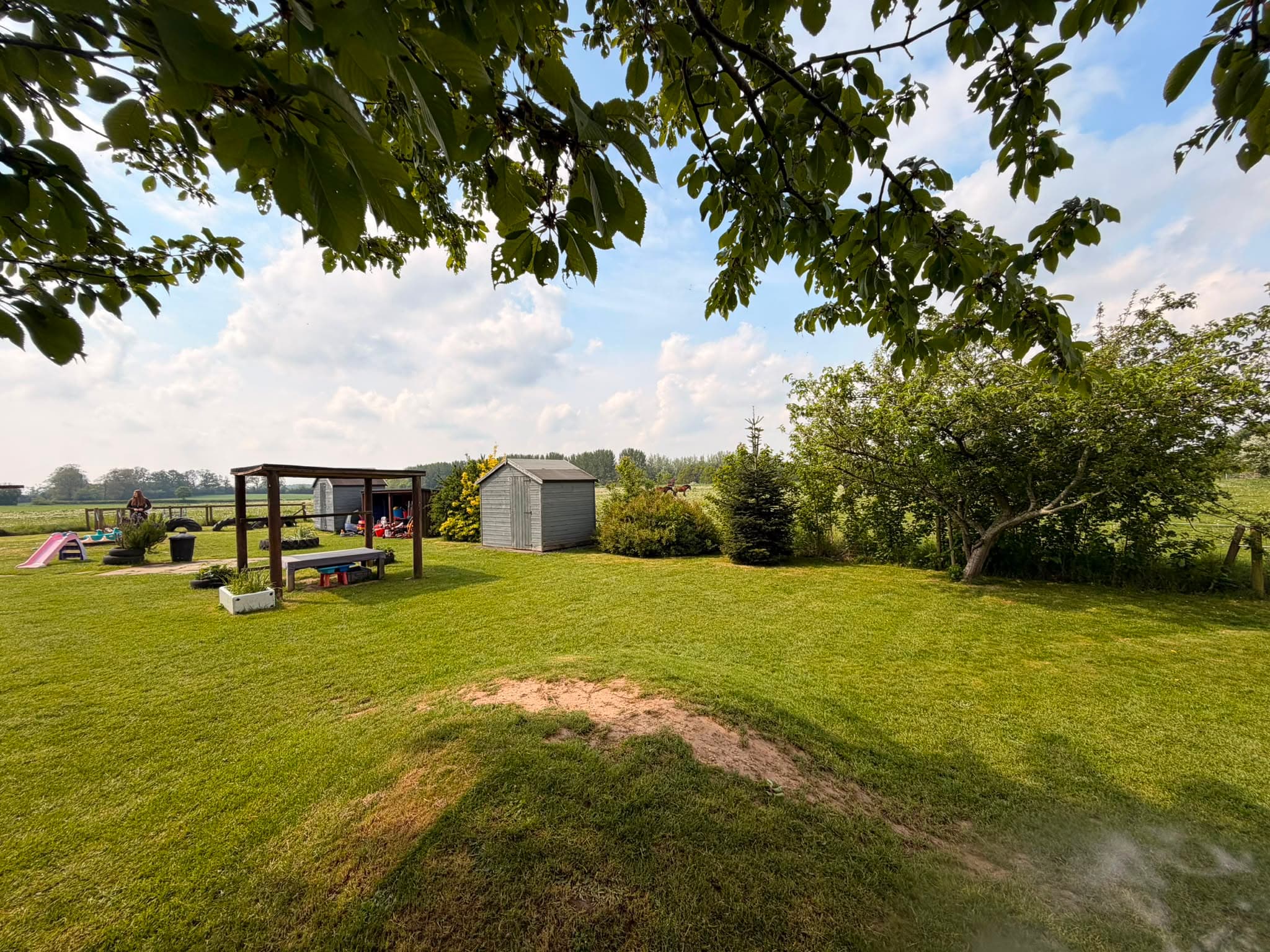 Nursery garden with a wooden climbing frame, slide and play house framed by trees and countryside
