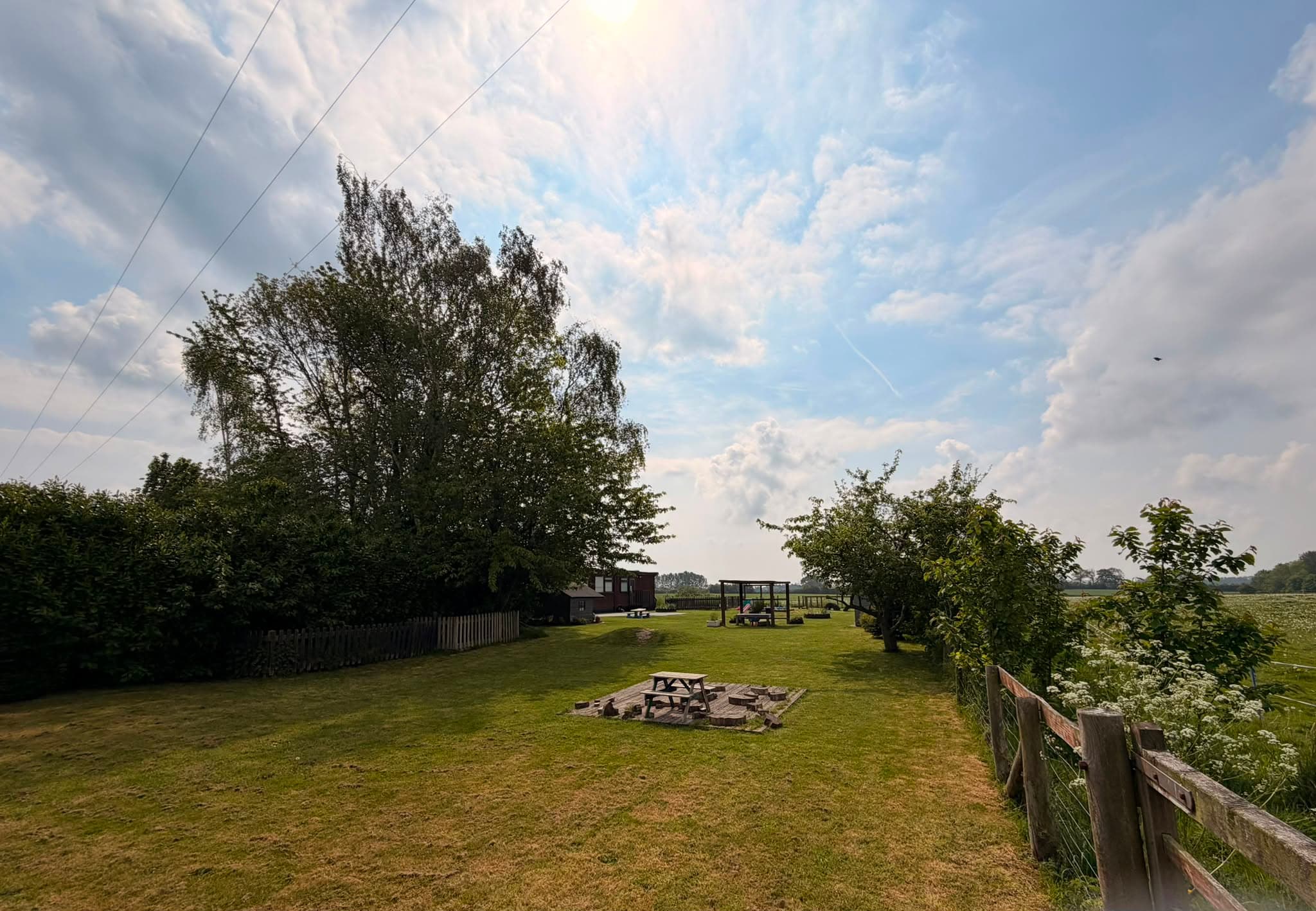 Large grassed nursery garden bordered by mature trees and hedgerows with views over open fields