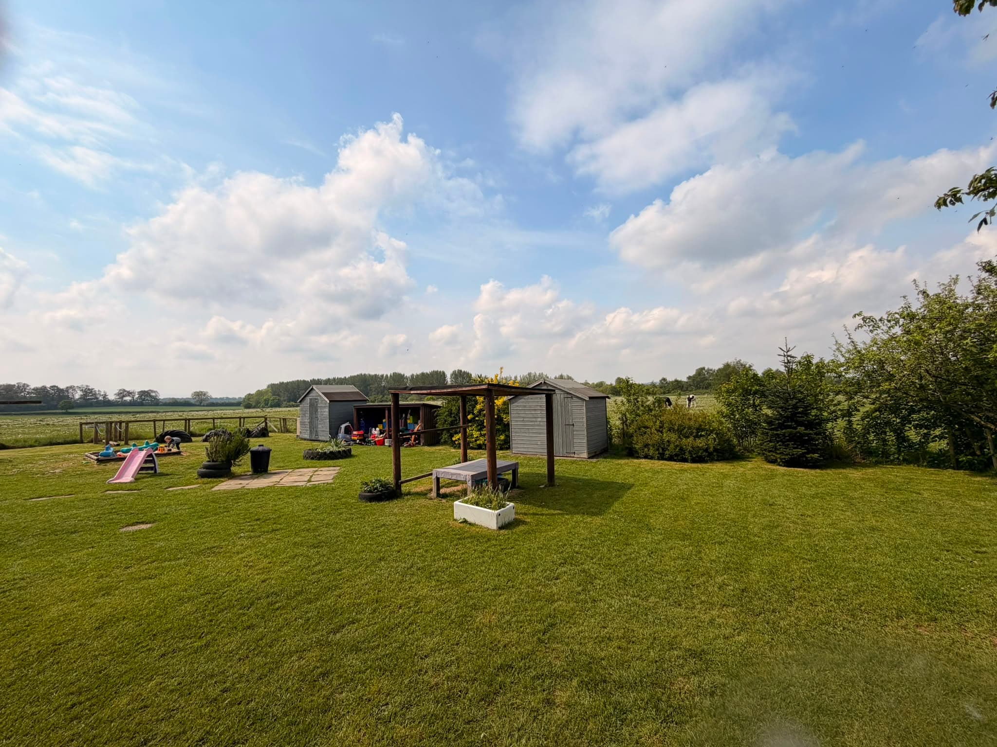 Nursery outdoor play area with a wooden playhouse and shaded canopy beside open Shropshire fields