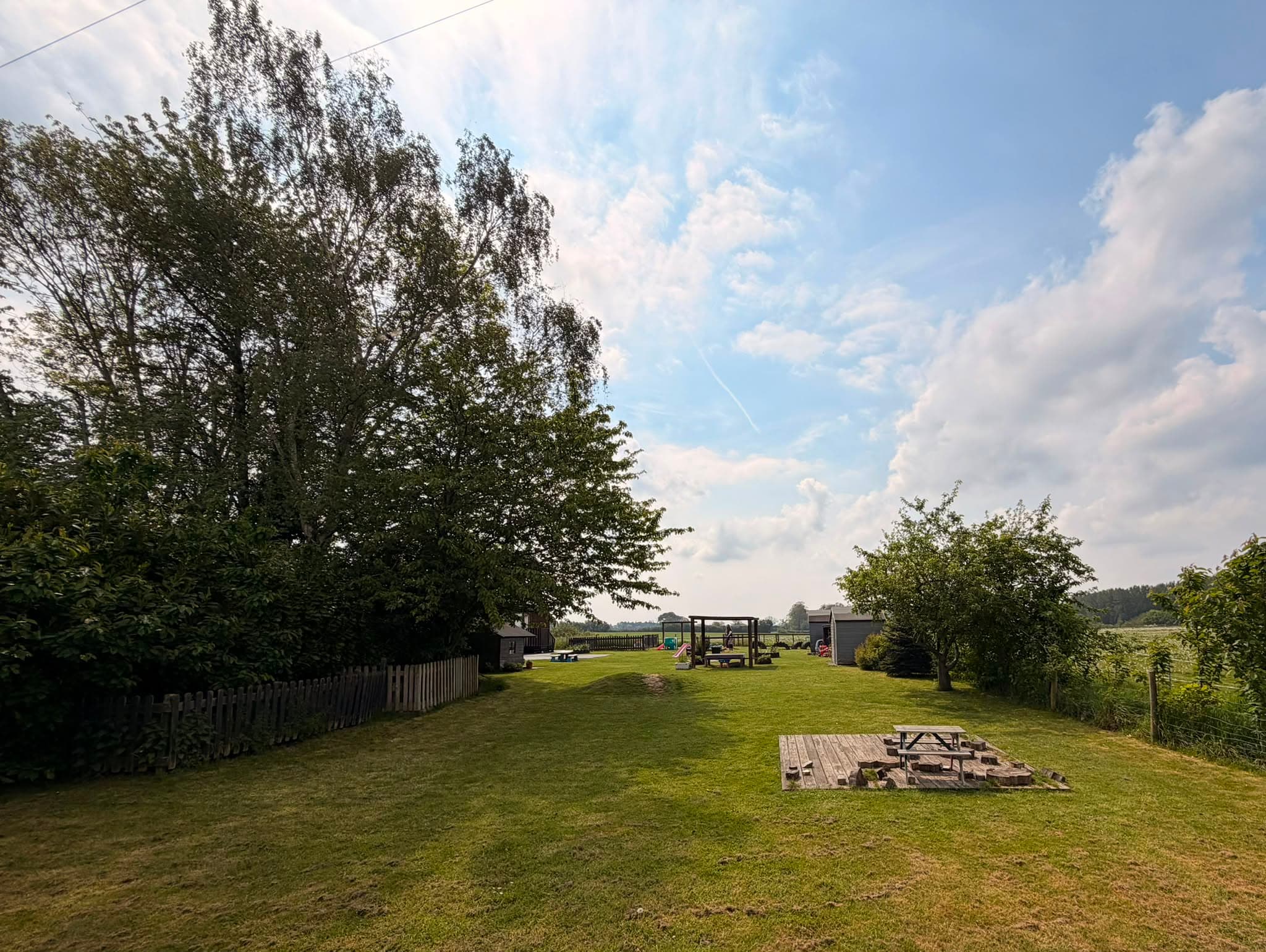 Spacious nursery garden with tall mature trees, a picnic bench and countryside views beyond the fence